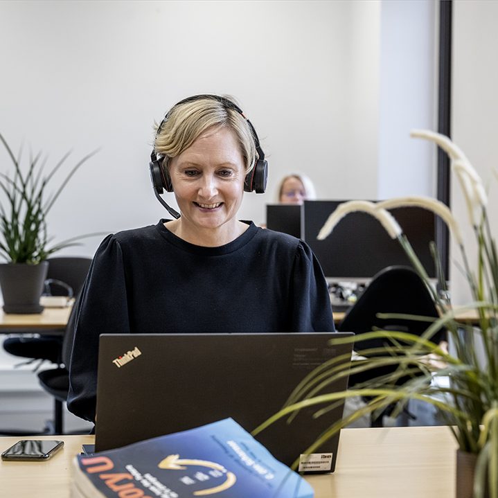 Billede af kvinde der sidder foran sin bærbar med hovedtelefoner på.