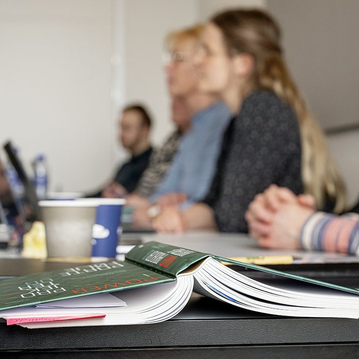 En bog i fokus, med koncentrerede studerende i baggrunden