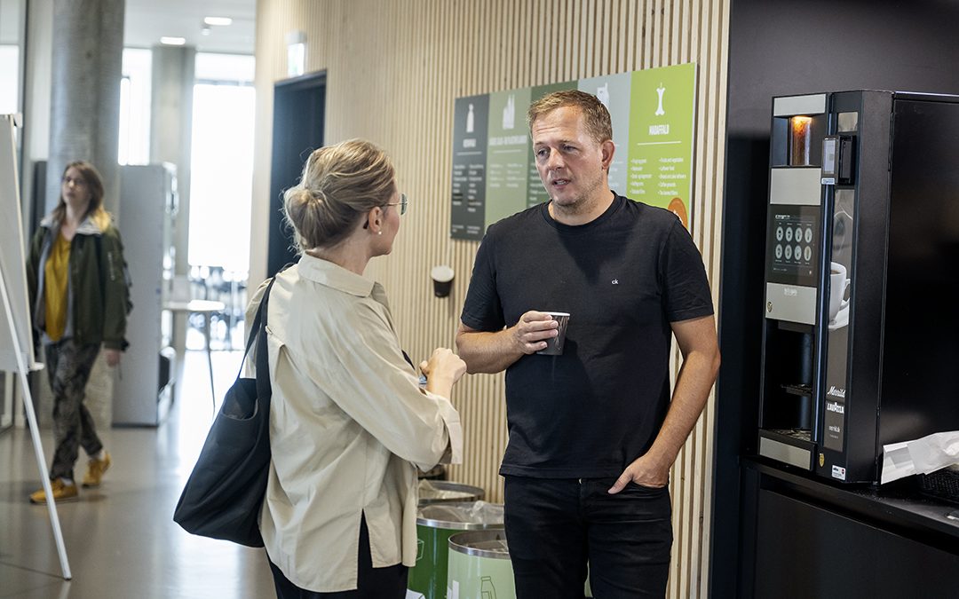 To studerende der snakker henover kaffemaskinen.