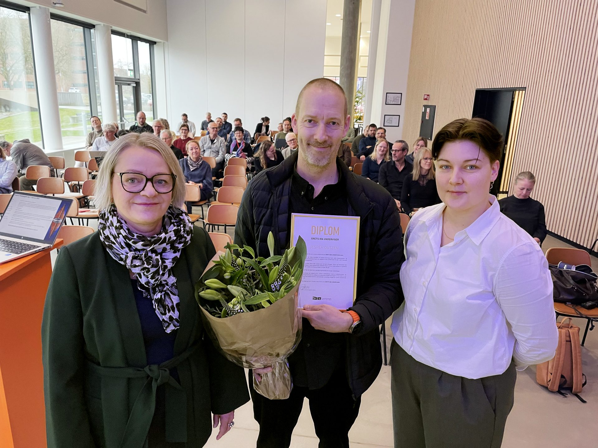 Jesper Outzen i auditoriet med en buket blomster og sin pris for Årets IBA Underviser